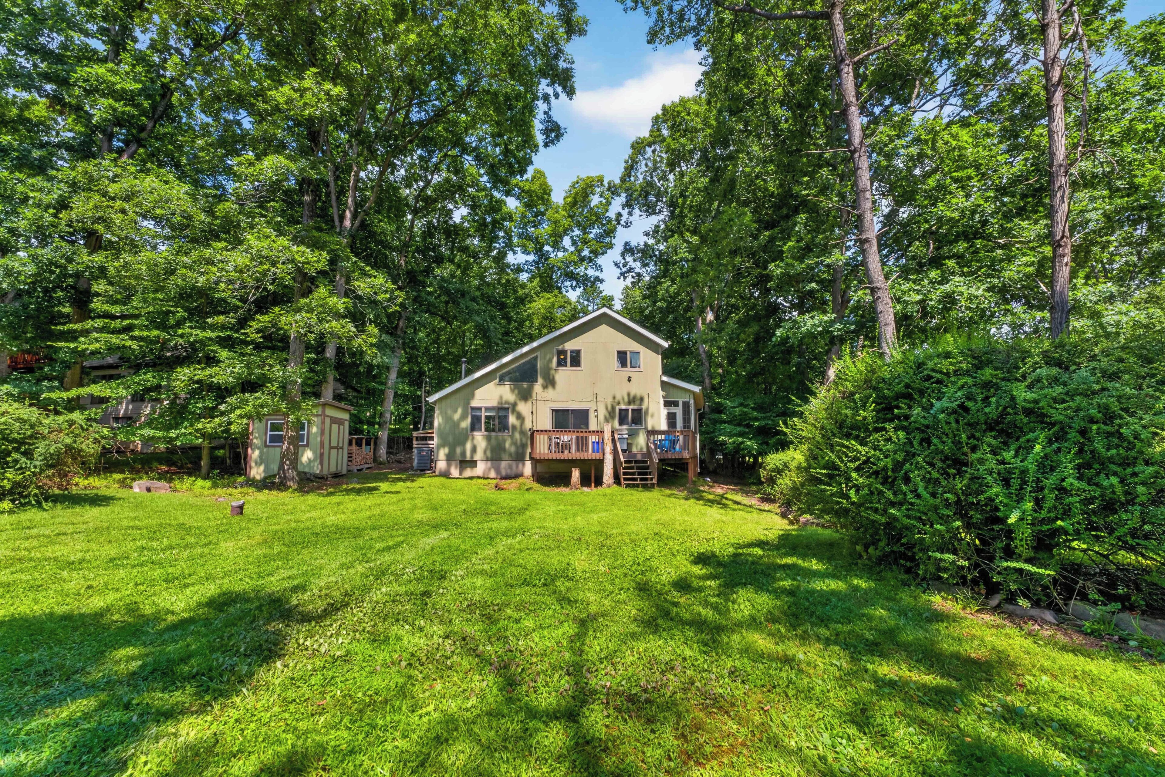 A two-story house with a deck, surrounded by a well-maintained lawn and dense trees.