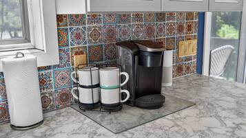 A kitchen with a marble countertop, a coffee maker, a kettle, and a paper towel holder.