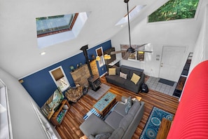 A spacious living area with a high ceiling, a fireplace, a sofa, and a dining table. - Cozy 2BD 2BA Hideaway w/ Pond Views & Firepit (East Stroudsburg)