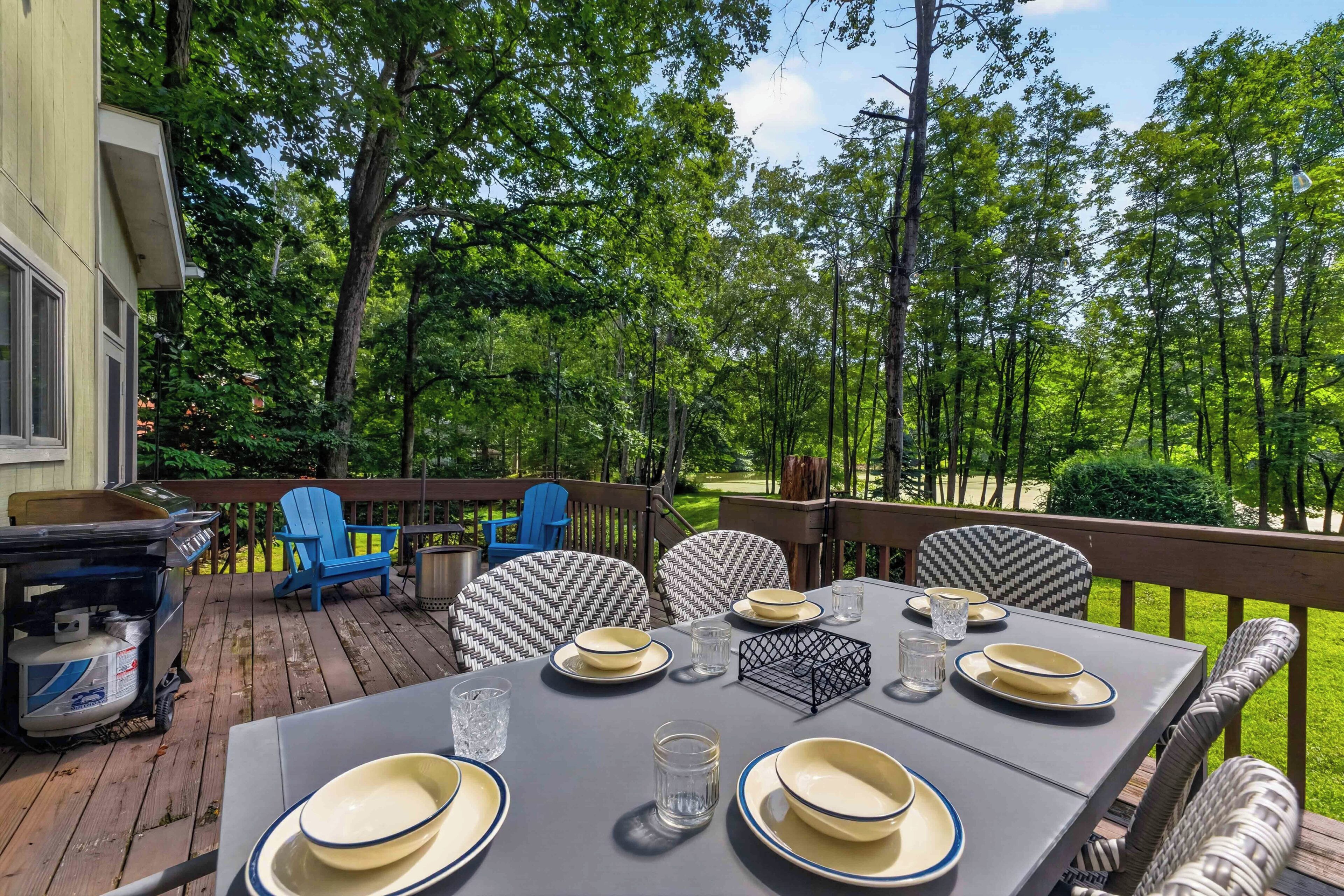 An outdoor deck with a table set for dining, surrounded by chairs and a grill.