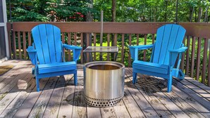 Une terrasse en bois avec deux chaises Adirondack bleues et un poêle en métal.