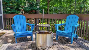 A wooden deck with two blue Adirondack chairs and a metal stove.