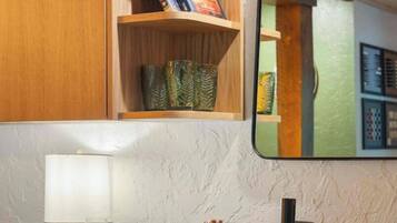 A kitchen with a wooden shelf, a mirror, a countertop with a glass of wine, and a fruit platter.