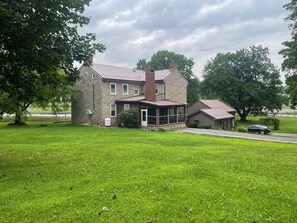 A two-story stone house with a large front lawn and a garage. - Beautiful Old Stone Mansion (Williamsburg)