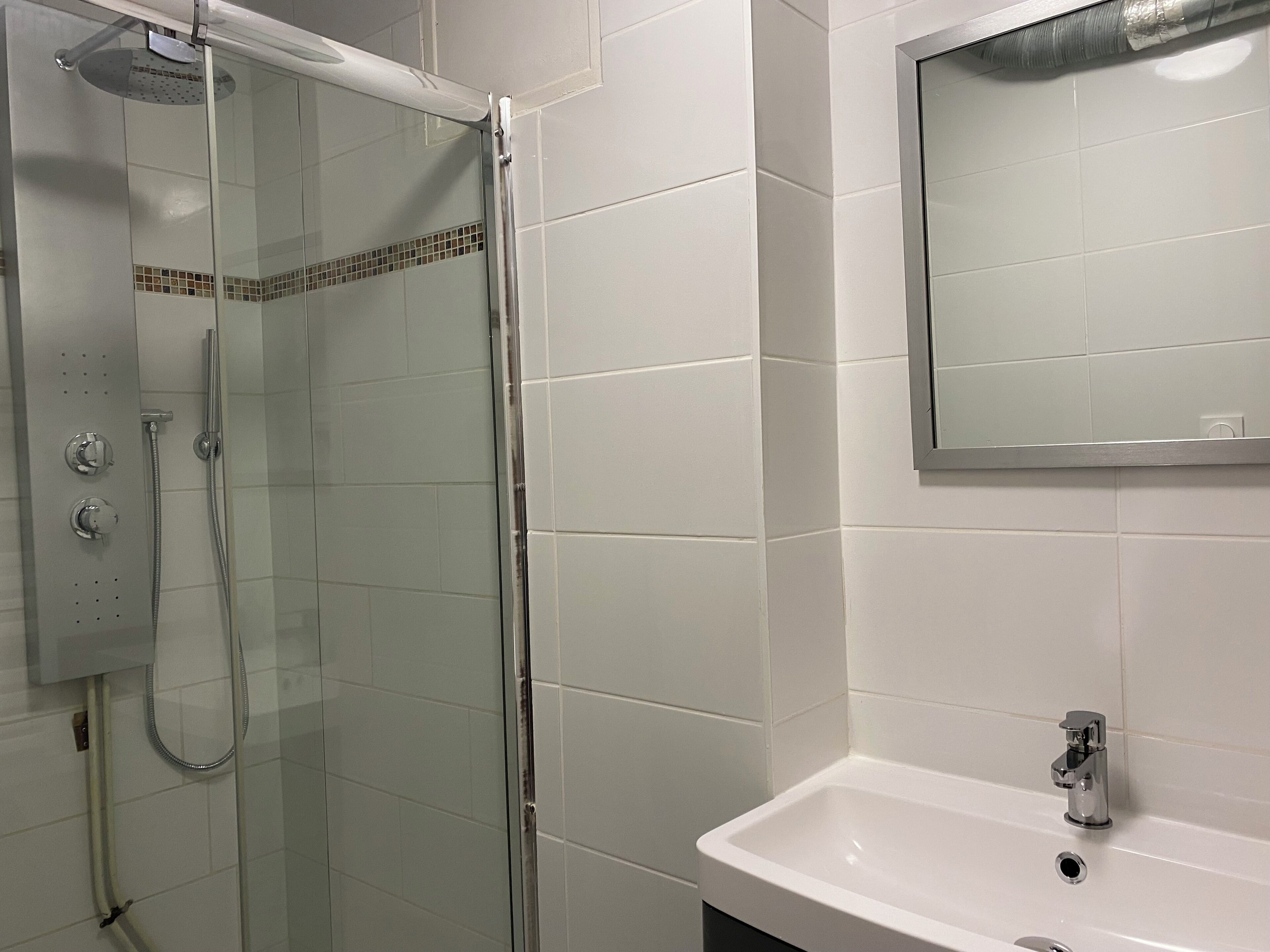 A bathroom with a glass-enclosed shower, a sink, and a mirror.
