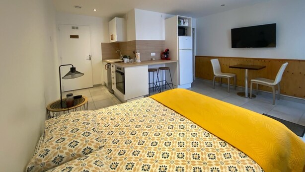 A compact hotel room with a bed, kitchenette, seating area, and a TV. - Apartment in Downtown Chalamont (Chalamont)