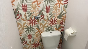 A small bathroom with a toilet, a toilet paper holder, and a shower curtain with a floral pattern. - Apartment in Downtown Chalamont (Chalamont)