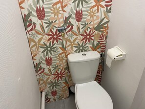 Ein kleines Badezimmer mit Toilette, Toilettenpapierhalter und einer blumigen Duschvorhang.