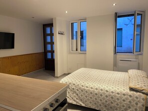Ein Schlafzimmer mit einem Bett, einem hölzernen Kopfteil, einem an der Wand montierten Fernseher und einem Fenster mit Blick ins Freie.