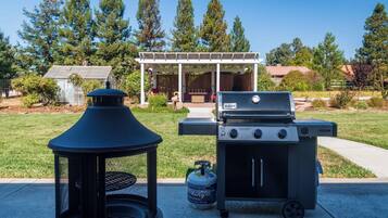 A barbecue grill with a gas tank, a lantern, and a pergola in a backyard.