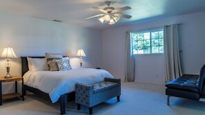 A bedroom with a bed, two bedside lamps, a ceiling fan, a window with curtains, a chair, and a small table. - Sea Rock Ranch by Avantstay Spa + Firepit + Game Room Paso Robles Wine Country (Templeton)