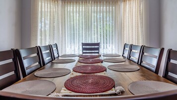 Una mesa de comedor con seis sillas, un camino de mesa tejido en el centro y vistas a través de cortinas traslúcidas.