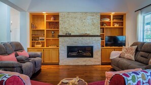 A living room with a stone fireplace, wooden shelves, two leather sofas, and a television. - Sea Rock Ranch by Avantstay Spa + Firepit + Game Room Paso Robles Wine Country (Templeton)