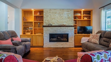 Una sala de estar con chimenea de piedra, estantes de madera, dos sofás de cuero y un televisor.