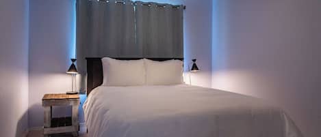 Un dormitorio con cama, dos lámparas de noche, una mesita de noche y una ventana con cortinas.