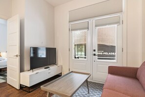 Ein modernes Hotelzimmer mit Fernseher, einem kleinen Tisch, einer Couch und einer Tür mit Blick auf ein Theater.