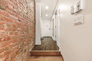 A narrow hallway with a brick wall on one side and a white wall on the other, leading to a door at the end. - Cozy Montreal 1BR • Steps to Old Port (Montreal)