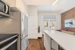 A modern kitchen with stainless steel appliances, a white countertop, and a brick accent wall. - Cozy Montreal 1BR • Steps to Old Port (Montreal)