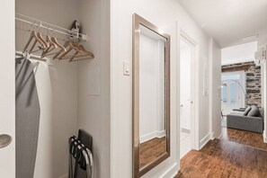 A hallway with a wooden door, a coat rack with hangers, and a glimpse of a living area with a sofa and a stone wall. - Modern 1BR • Walk to Old Port (Montreal)