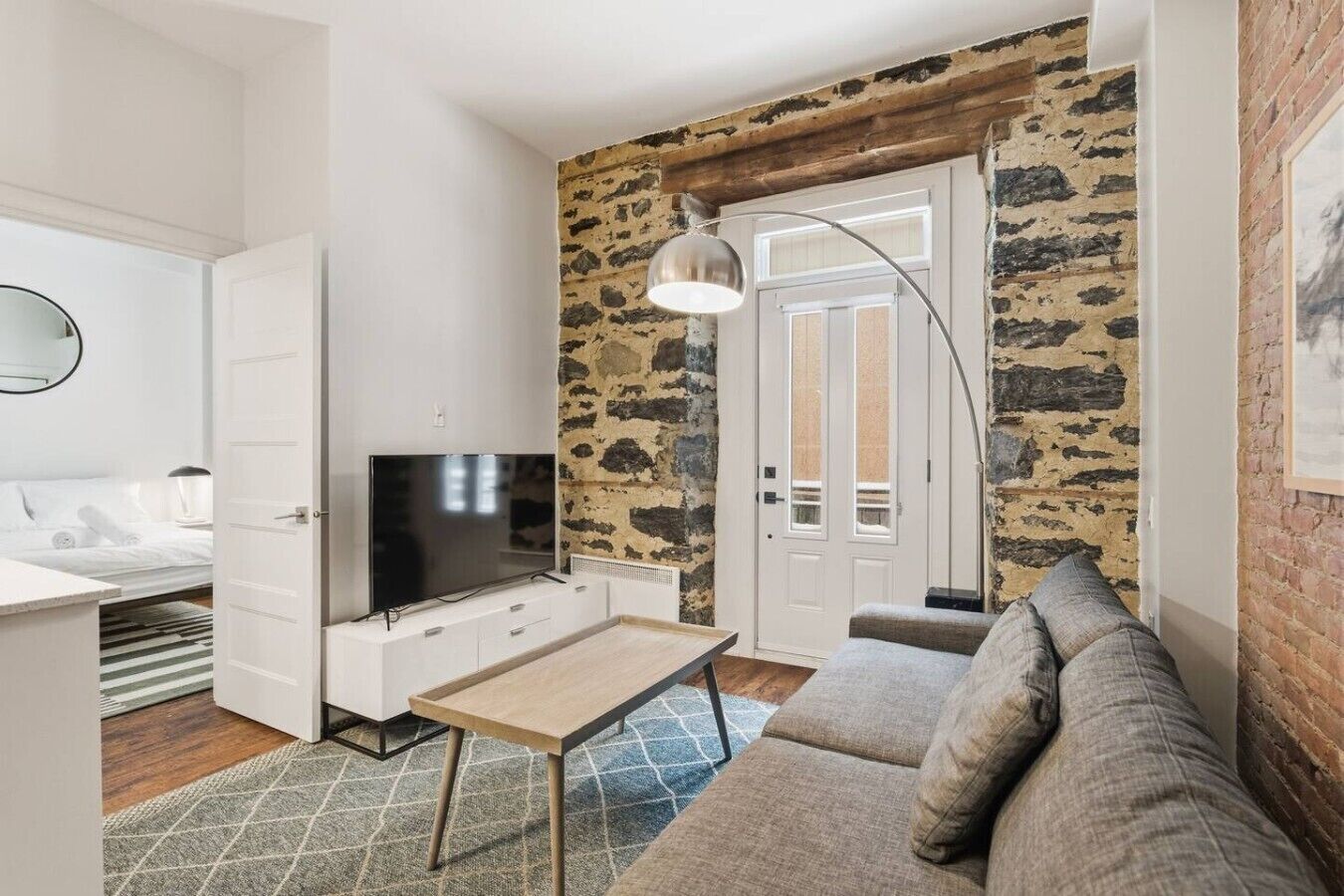 A modern living room with a television, a sofa, a coffee table, and a stone accent wall.