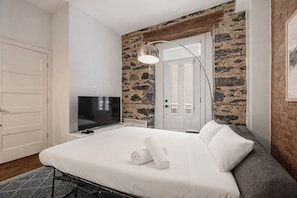 A hotel room with a bed, a television, a stone accent wall, and a door. - Modern 1BR • Walk to Old Port (Montreal)