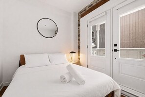 A white bed with a rolled towel, a bedside lamp, and a round mirror on the wall. - Modern 1BR • Walk to Old Port (Montreal)