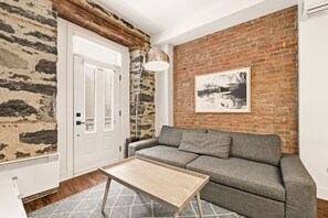 A room with a brick wall, a grey sofa, a wooden coffee table, and a white door. - Modern 1BR • Walk to Old Port (Montreal)