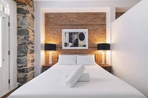 A hotel room with a brick wall, a bed with white linens, two bedside tables with lamps, and a framed artwork above the bed. - Modern Downtown Montreal 2-Bedroom • Steps to Old Port (Montreal)