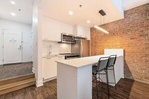 Une cuisine moderne avec des meubles blancs, des appareils en acier inoxydable et un mur d’accent en briques.
