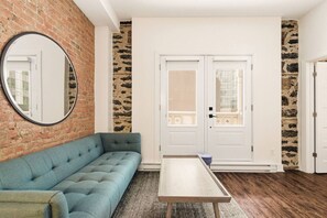 A room with a blue sofa, a small table, a mirror, and a door with a window. - Modern Downtown Montreal 2-Bedroom • Steps to Old Port (Montreal)