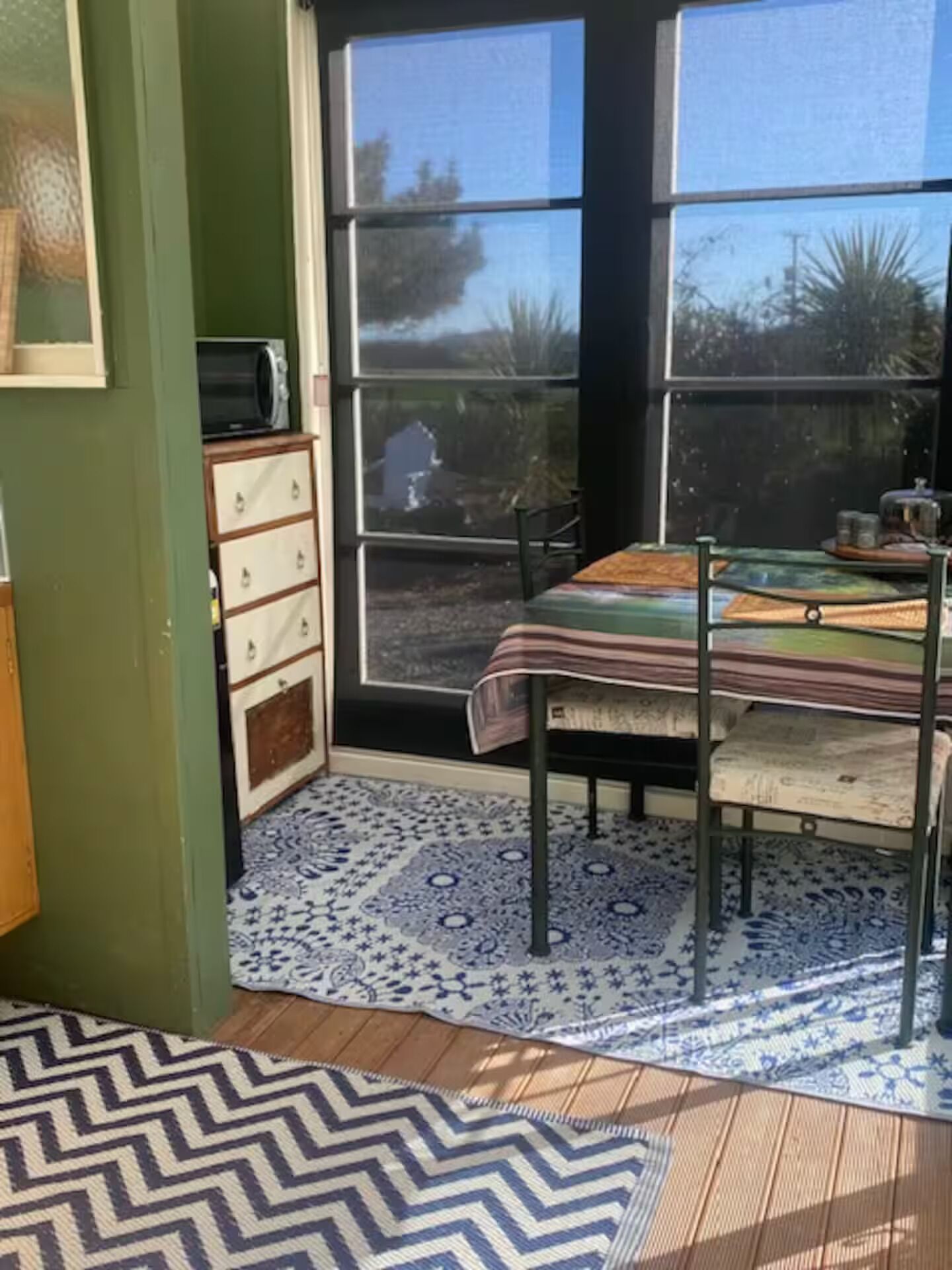 A room with a dining table, chairs, a patterned rug, a microwave, and a cabinet.