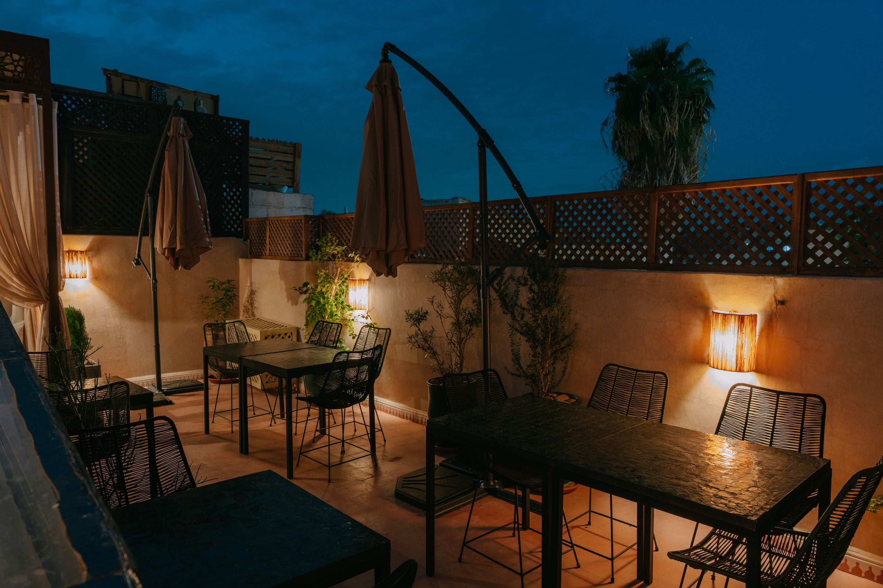 Un patio al aire libre con mesa y sillas, rodeado de plantas y sombrillas.