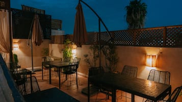 Un patio al aire libre con mesa y sillas, rodeado de plantas y sombrillas.