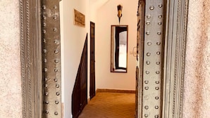 Corredor com porta de metal e janela, dando acesso a um quarto com piso ladrilhado.