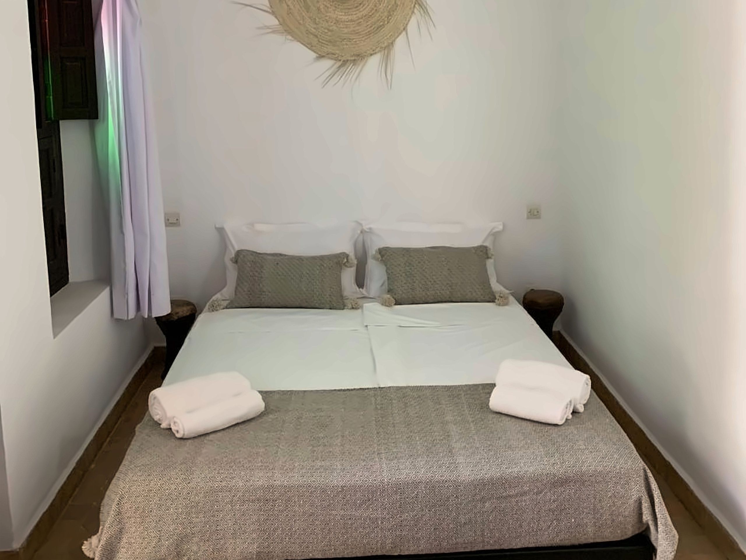 A single bed with a patterned bedspread, two pillows, and two folded towels.
