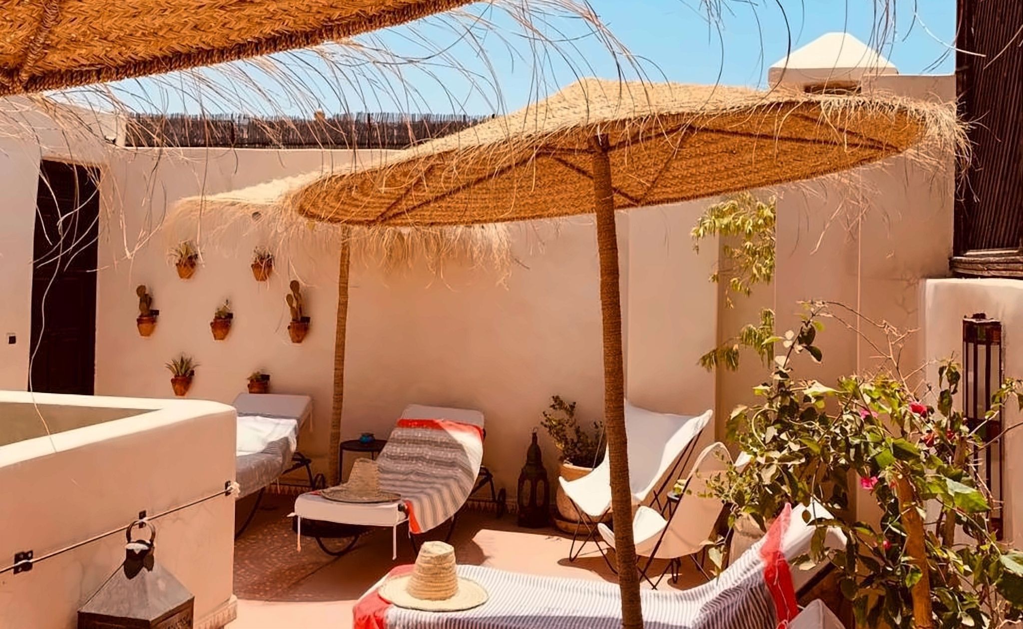 A cozy outdoor seating area with a thatched umbrella, a small table, and potted plants.