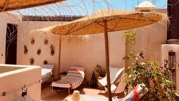 A cozy outdoor seating area with a thatched umbrella, a small table, and potted plants.