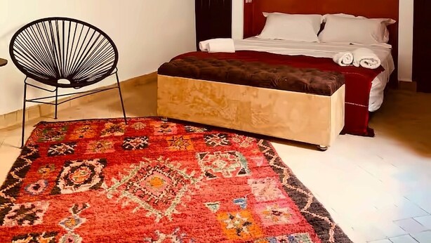 Quarto com cama, uma cadeira, tapete, quadro e duas luminárias pendentes.