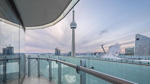 Ein Balkon mit Glasgeländer, der auf einen Stadtblick mit einem markanten Turm und modernen Gebäuden zeigt.