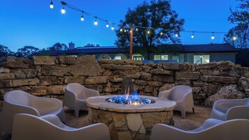 A stone fire pit with chairs around it, a stone wall, and string lights in the background.