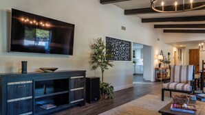 A modern living room with a flat-screen TV, dark wood entertainment unit, a potted plant, and a patterned wall. - Na Hoku Ranch by Avantstay Spanish Hacienda + Spa + Court 5.5 Acres Near Paso (Atascadero)