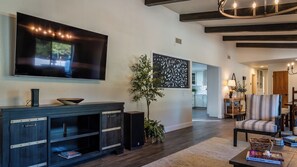 Ein modernes Wohnzimmer mit Flachbildfernseher, einer Unterhaltungseinheit aus dunklem Holz, einer Topfpflanze und einer Wand mit Muster.