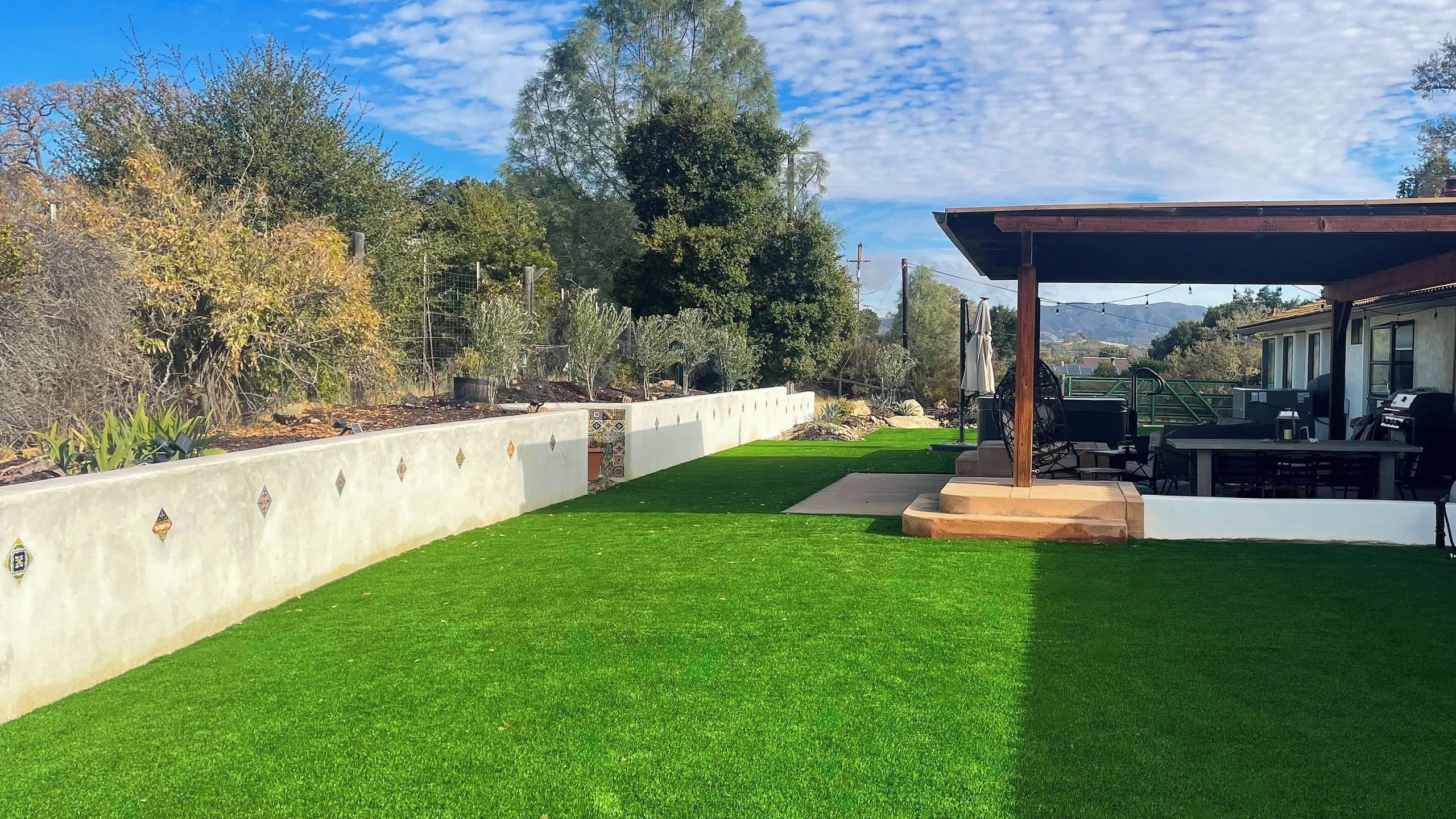 A well-maintained lawn with a patio area, outdoor seating, and a view of trees and hills in the background.