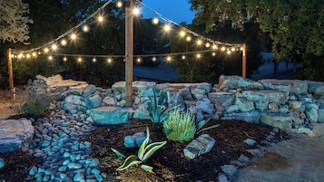 A landscaped garden with a stone wall, a variety of plants, and string lights.