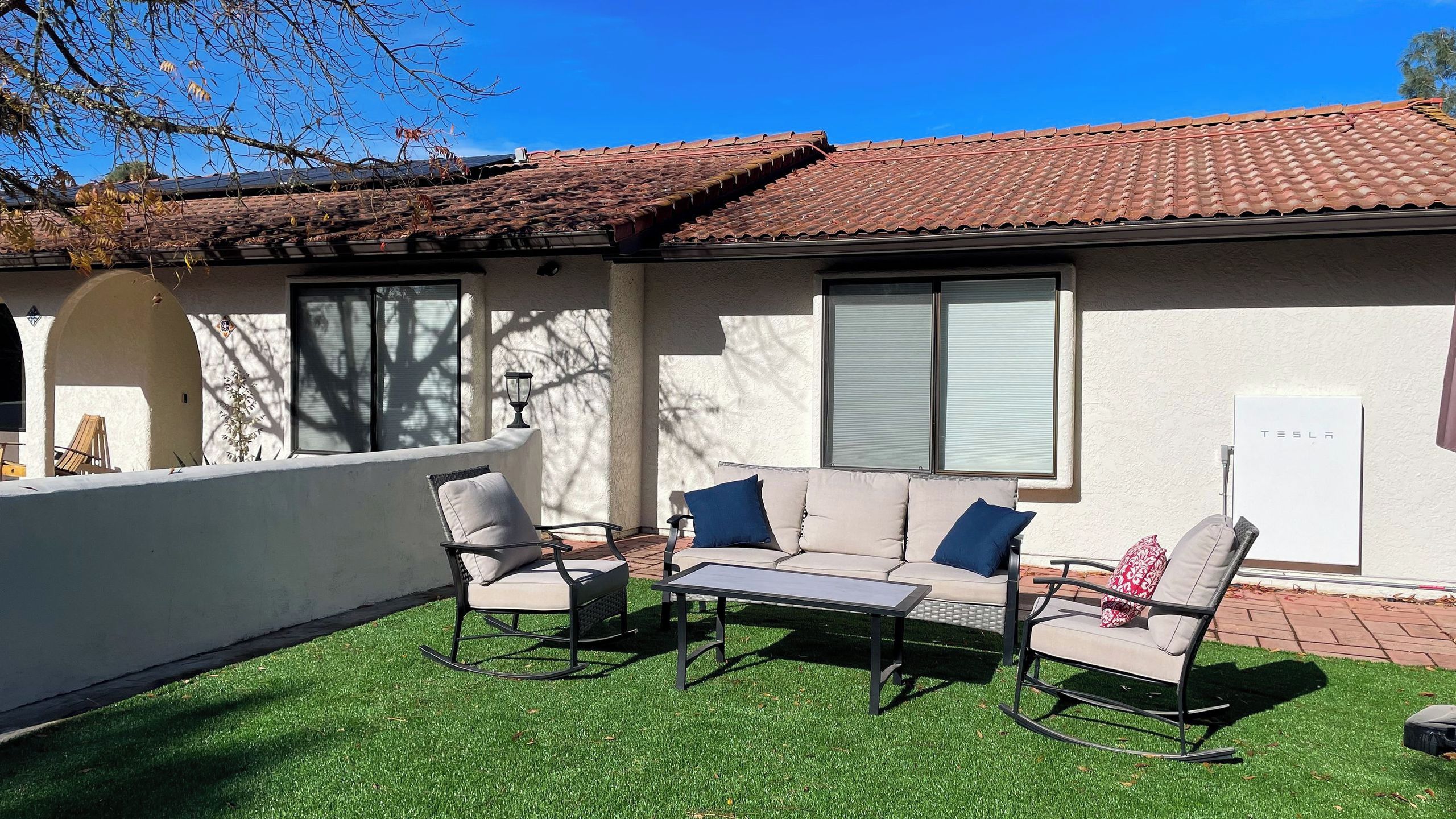An outdoor seating area with a sofa, chairs, and a table, surrounded by a white wall and a tiled roof.