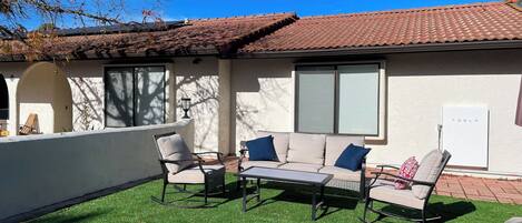 An outdoor seating area with a sofa, chairs, and a table, surrounded by a white wall and a tiled roof.