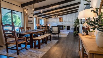 Un comedor amplio con una larga mesa de madera y sillas, una chimenea y una pared de ladrillo al fondo.