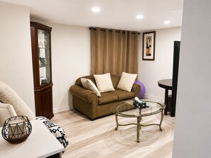 A living room with a brown sofa, a glass coffee table, a cabinet with glass doors, and a framed picture on the wall. - Maple Haven | Spacious 3BR Private Luxury Suite • Huge Yard • Sleeps 6 (Pickering)