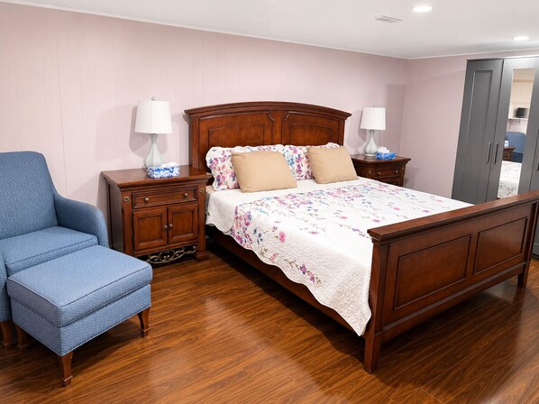 A bedroom with a wooden bed, a blue armchair, a nightstand with a lamp, and a dresser.