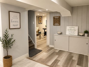A hallway with a staircase, a potted plant, and a cabinet with a sign.